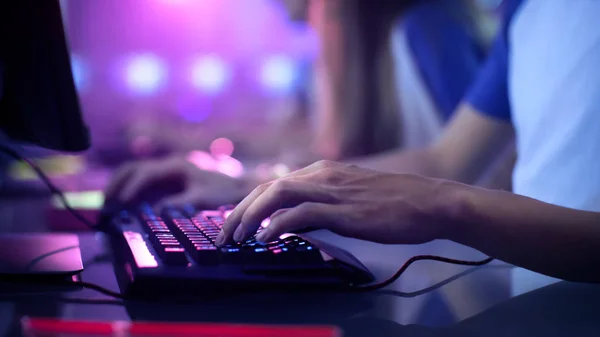 Close-up of a player's hands on a glowing backlit mechanical keyboard under blue and purple club lighting